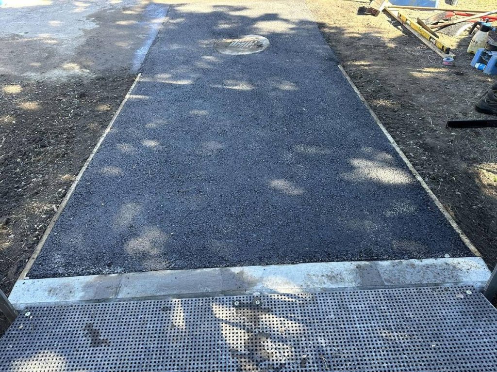 Finished asphalt patch around a pit, level with the surrounding surface